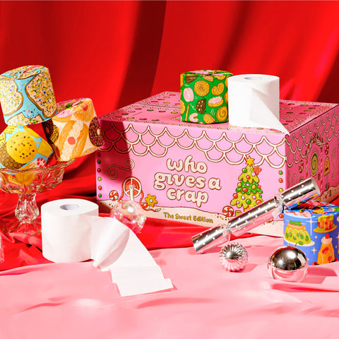 Colourful 'Who Gives a Crap' Sweet Limited Edition box decorated with candy illustrations, with toilet paper rolls stacked on top.